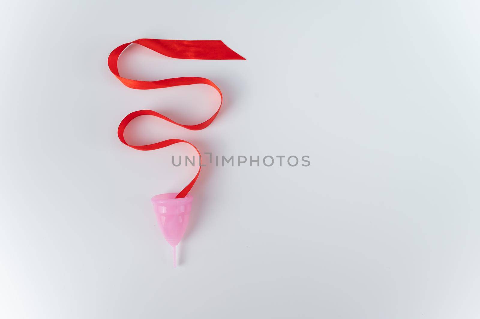 Pink menstrual cup and red satin ribbon on a white background. Copy space.