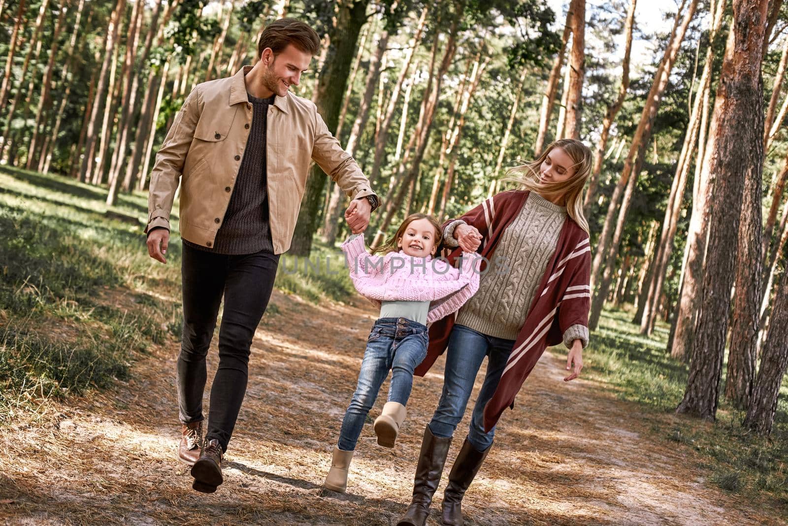 Young parents with little daughter in autumn forest. Mom and dad holding baby girl