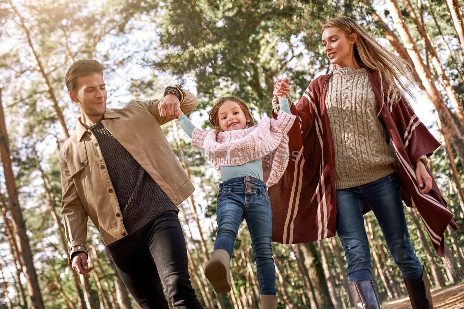 Young parents with little daughter in autumn forest. Mom and dad holding baby girl. Bottom view