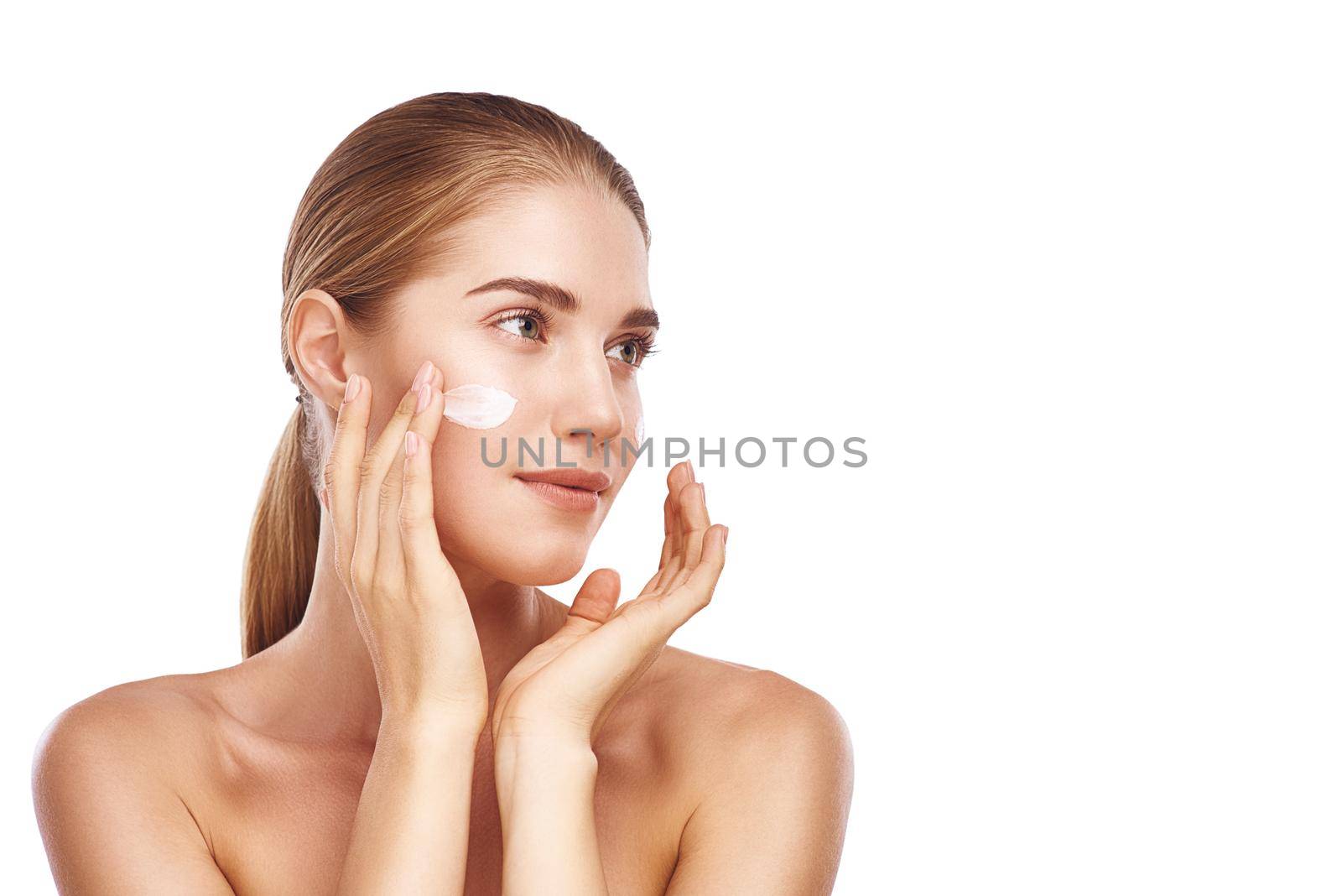 Beautiful womans left cheek with facecream close up studio photo on white background. Light hair, grey eyes