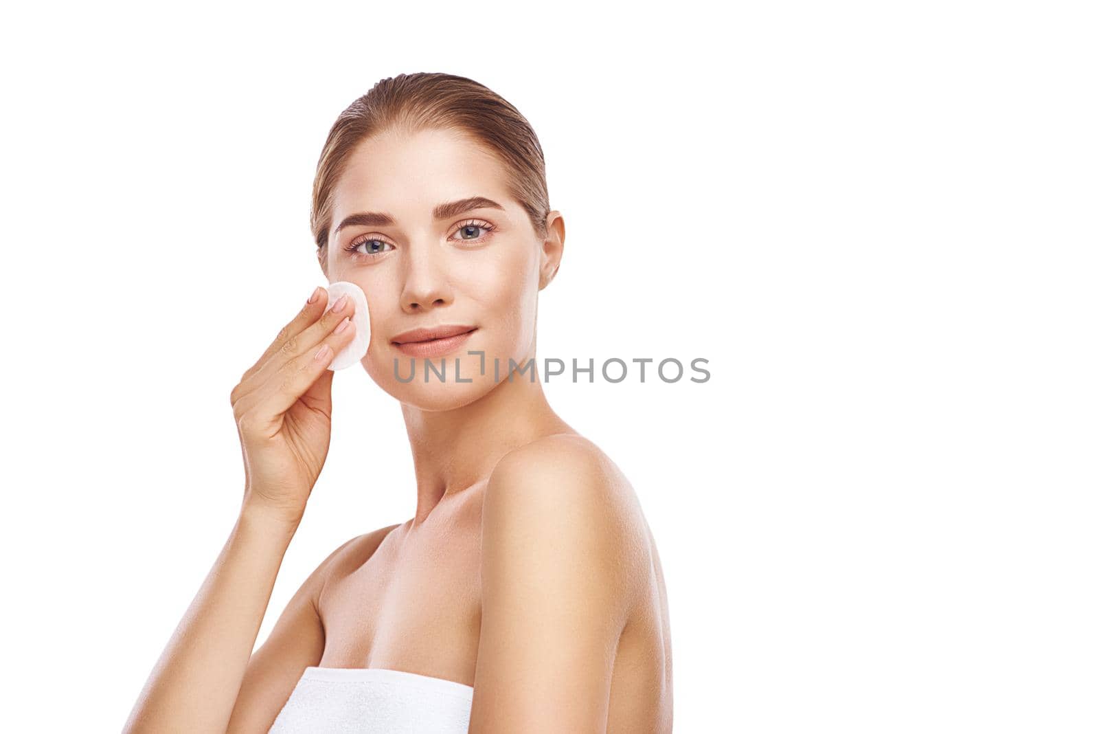 Beautiful woman cleans her face with sponge, she wearing white towel, close-up studio photo on white background. Light hair, grey eyes