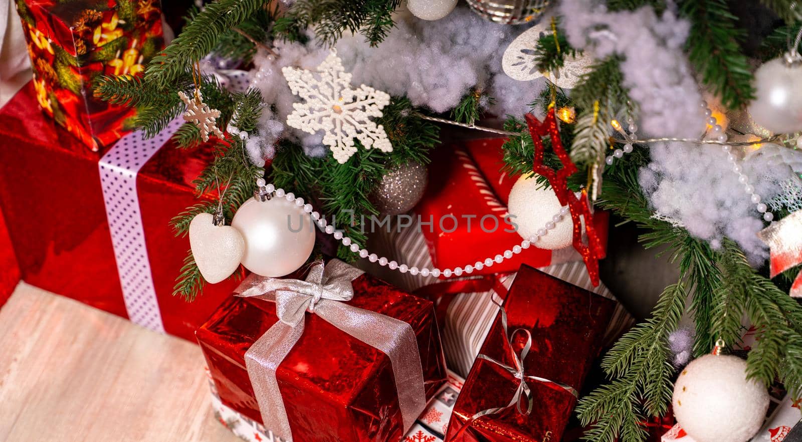 Wrapped gifts under Christmas tree. Many boxes of presents on floor near coniferous tree. Concept of holidays and surprises