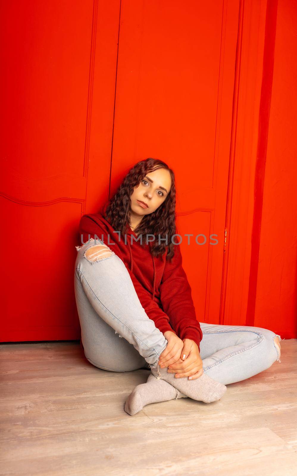 Young woman sitting on floor. Curly brunette poses near red wall