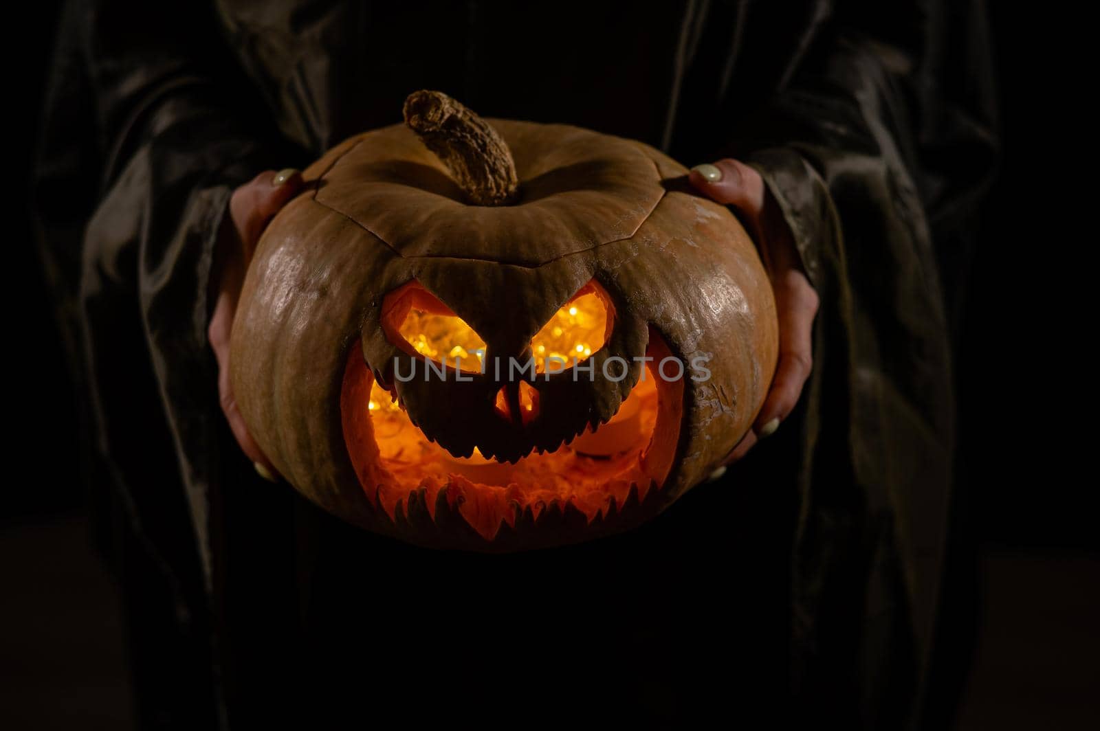 The witch is holding a pumpkin jack o lantern glowing in the dark. Halloween