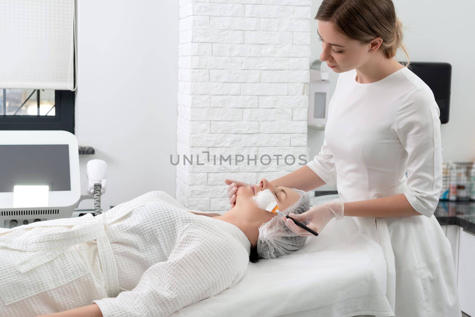 Mature woman receiving wwhte facial mask in spa beauty salon. Concept of skin care for older people by Mariakray