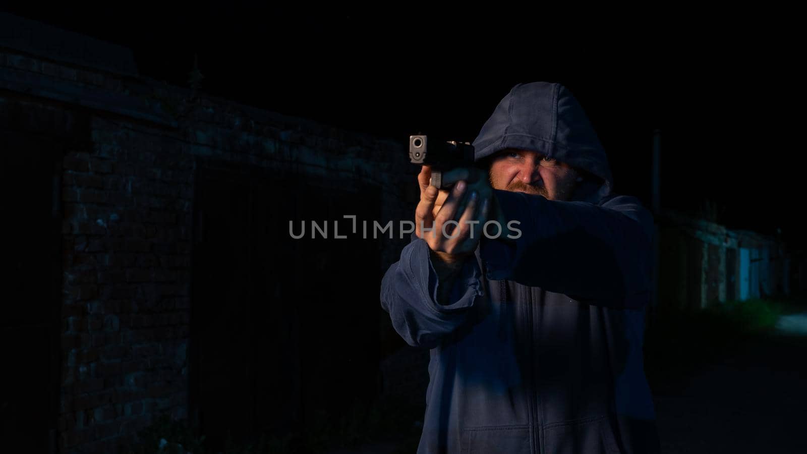 Caucasian man in a hood shoots a pistol