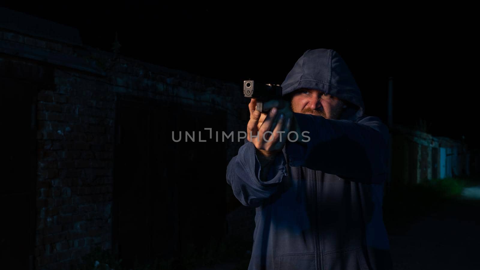 Caucasian man in a hood shoots a pistol. by mrwed54