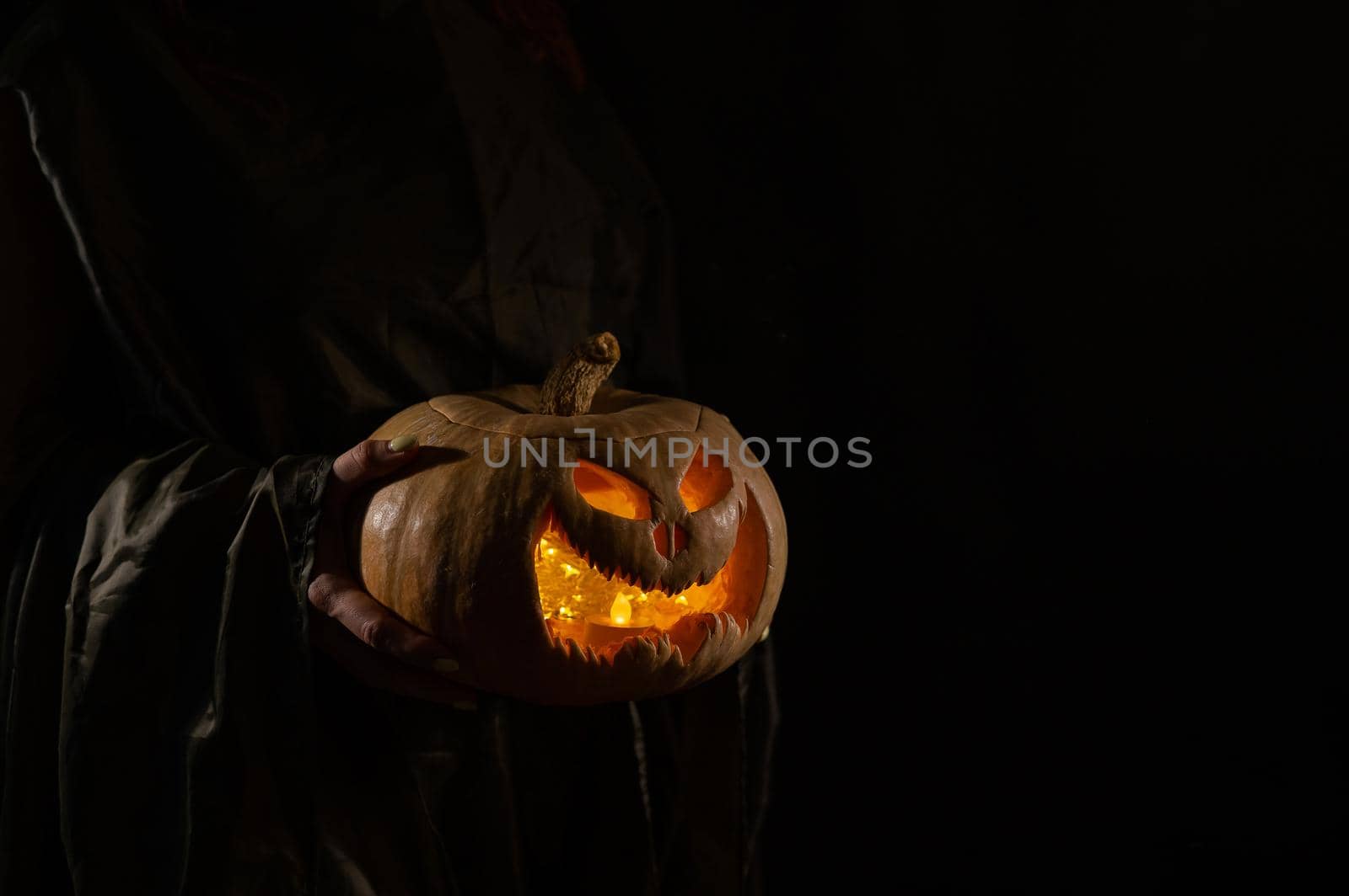 The witch is holding a pumpkin jack o lantern glowing in the dark. Halloween