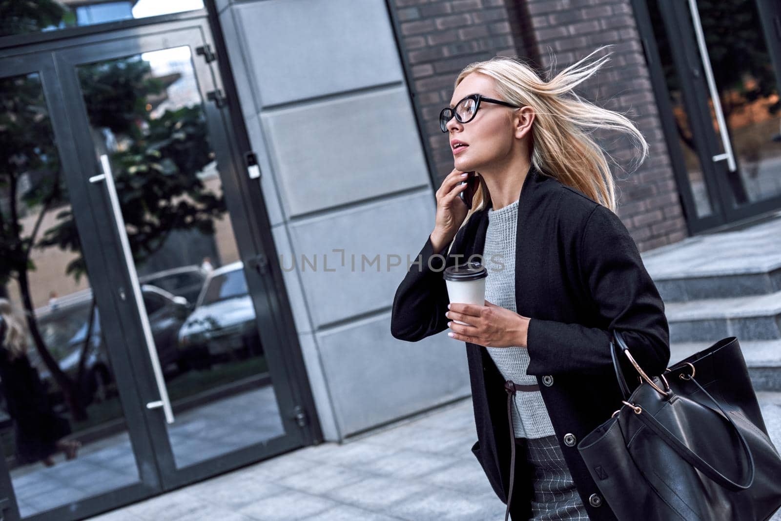 Young stylish woman talking by smartphone. She walks with morning coffee by friendsstock