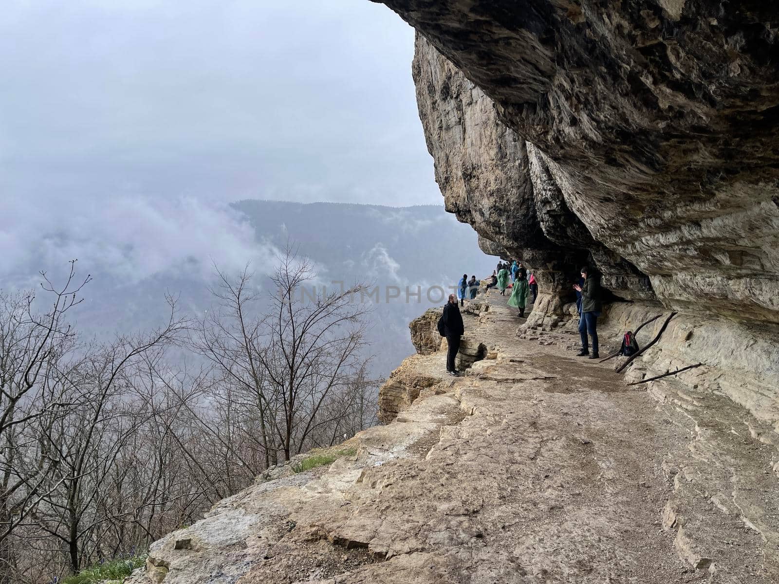 Tourists on huge cliff with spectacular view of nature. Group of people on high rock in foggy and cloudy weather.