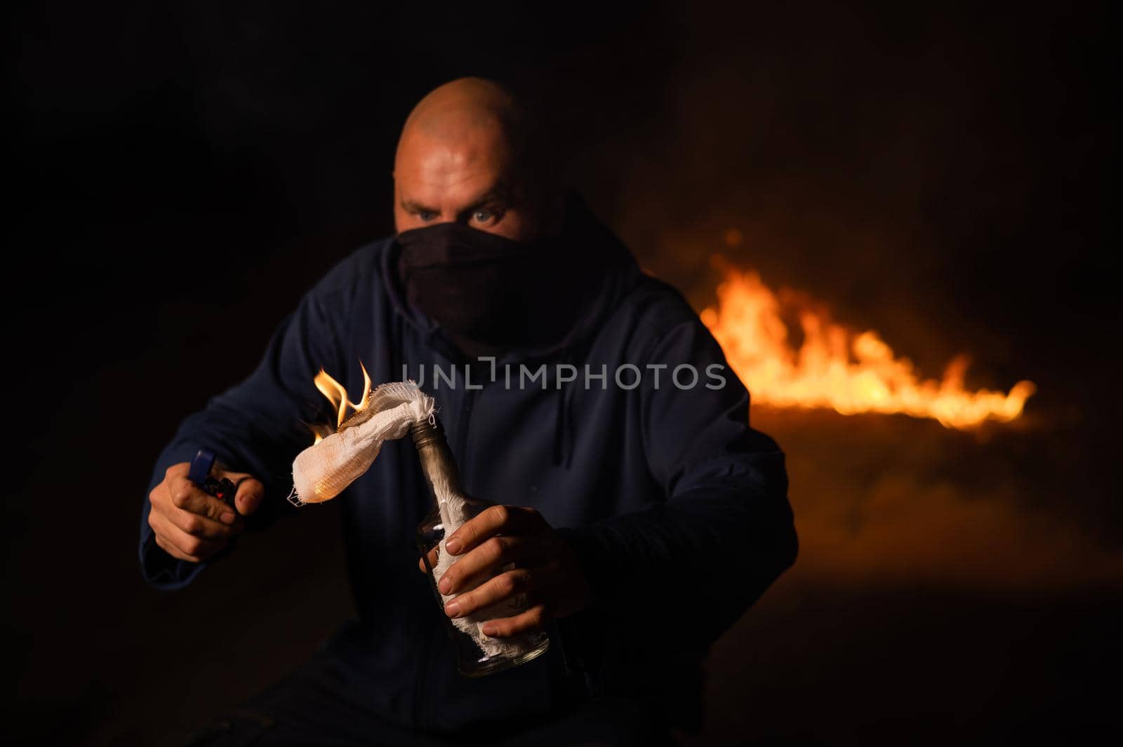 A masked man is holding a burning bottle. Molotov cocktail