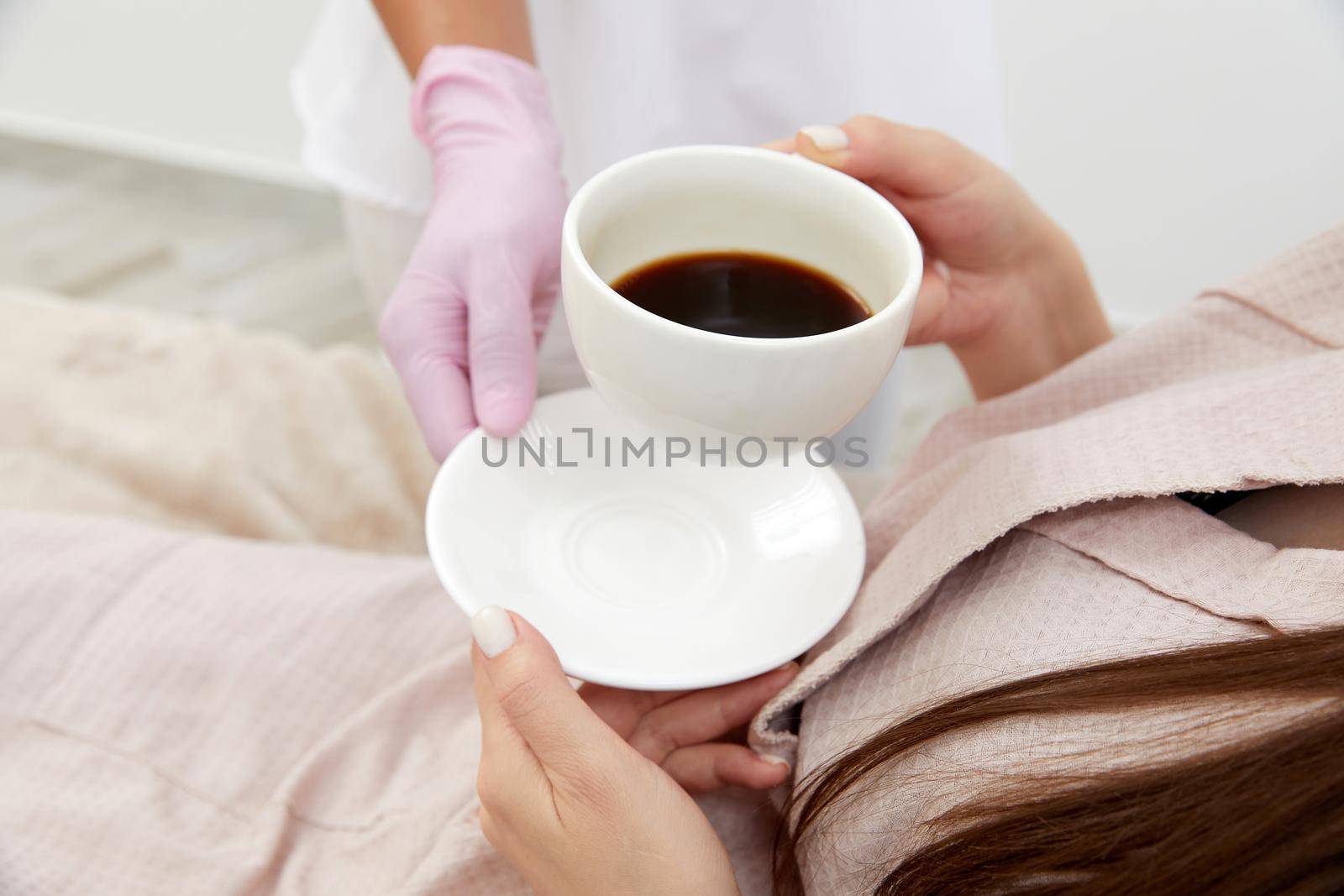 Beautician serving cup of coffee to her client after body treatment in beauty salon. Relaxing with beverages on cosmetic bed. Beauty , pleasure concept