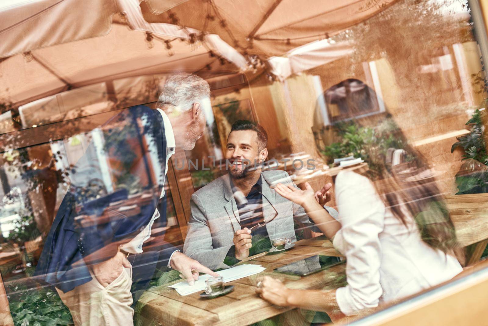 Business lunch. Three people in the restaurant sitting at table discussing project smiling happy outside the window view. Team work concept by friendsstock