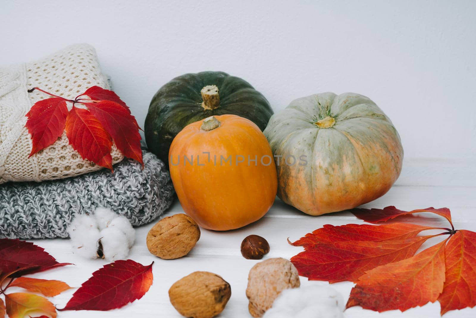 Autumn composition of sweaters and pumpkins lie on a wooden white table. by Rodnova