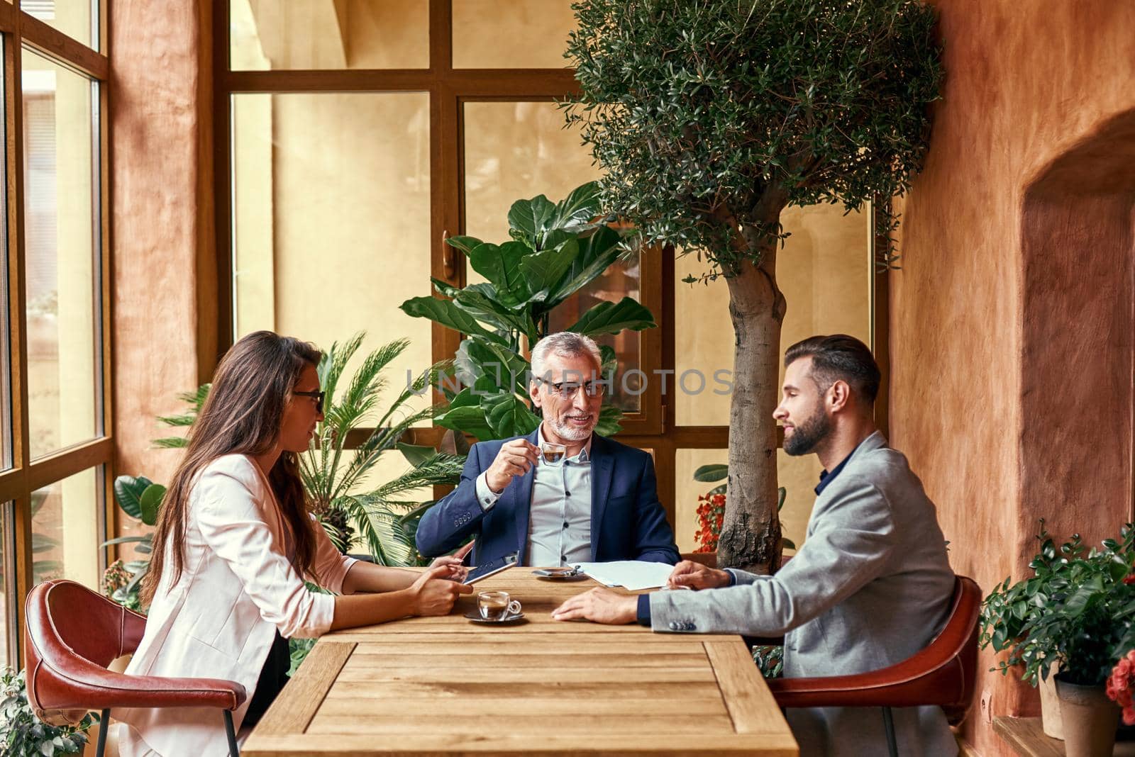 Business lunch. Three people in the restaurant sitting at table drinking hot coffee discussing project joyful. Team work concept