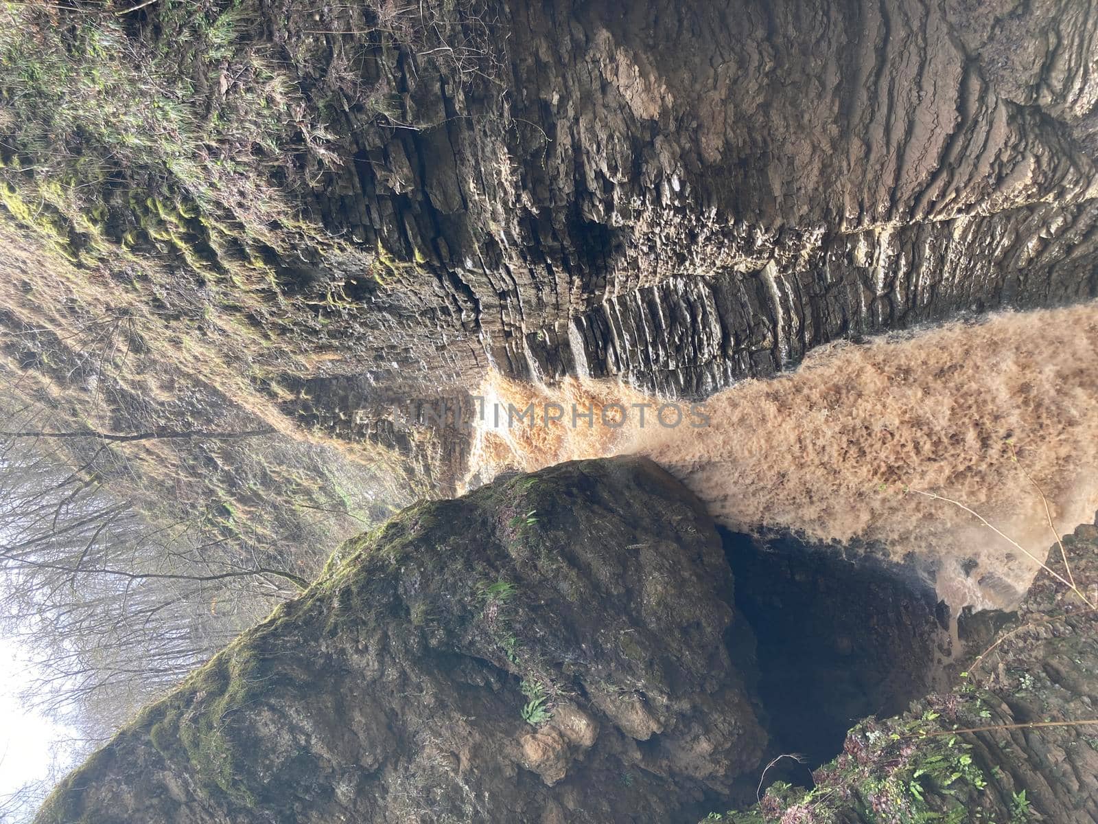 Beautiful landscape of powerful muddy waterfall in mountainous terrain. Dirty mountain waterway flows down and splashes. by epidemiks