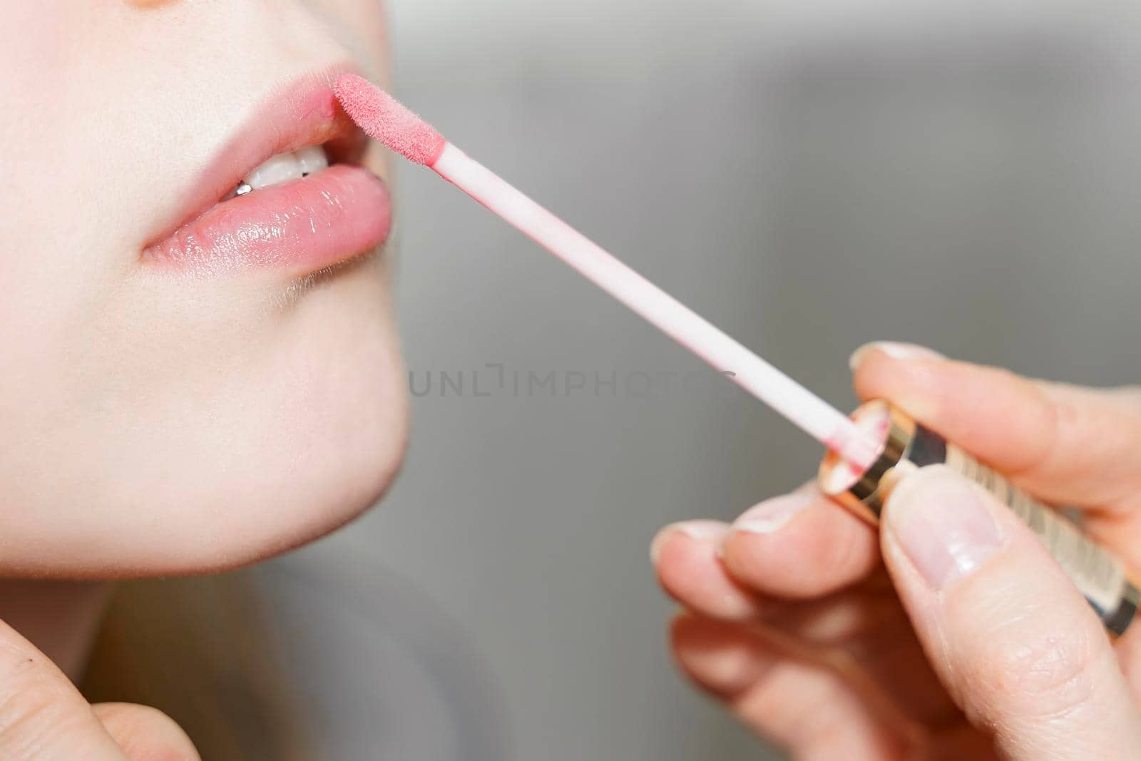 applying lip gloss to lips of a beautiful young woman close up