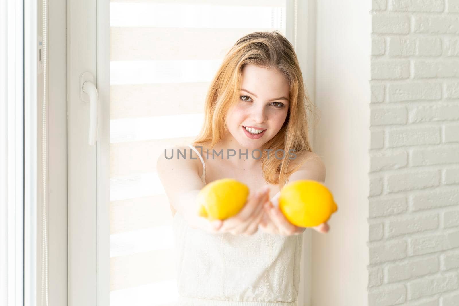 beautiful young woman in a white dress is holding two lemons and smiling. healthy lifestyle concept by Lena_Ogurtsova