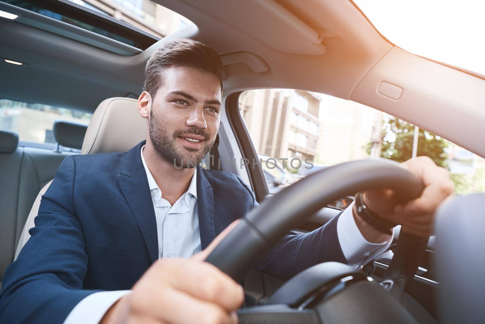 Portrait of joyful man driving car in formalwear and keeping hands at steering wheel.