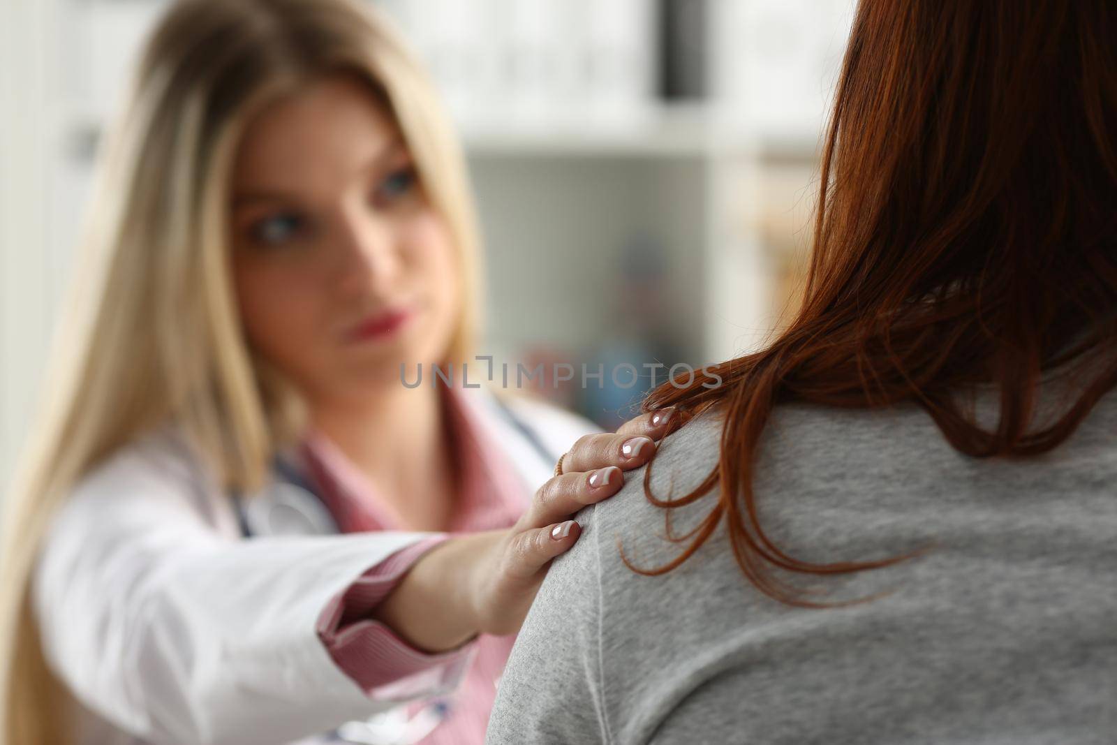 Handsome friendly female doctor talk with thankful female patient at office and greet her with hand on shoulder gesture. Welcoming friend trust physical healthy lifestyle exam interview concept