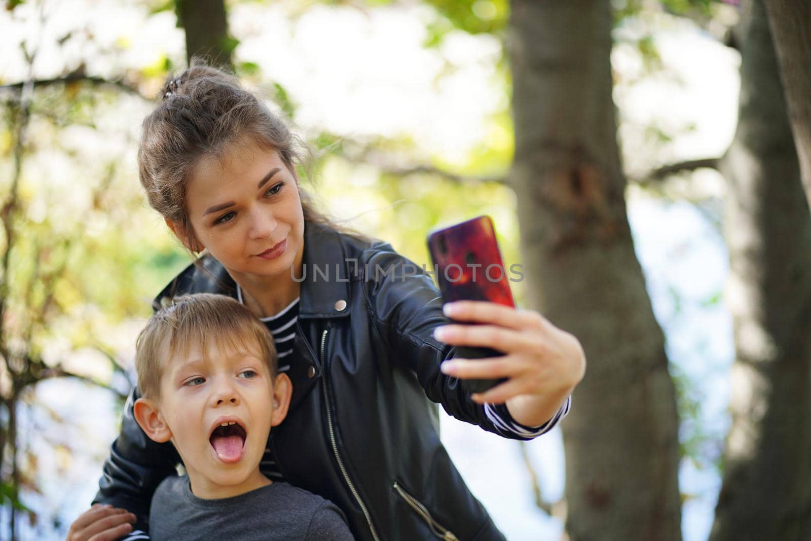 A young mother with her son takes a selfie. Smiling young woman with long hair and a child take a selfie with a smartphone, in the park by epidemiks