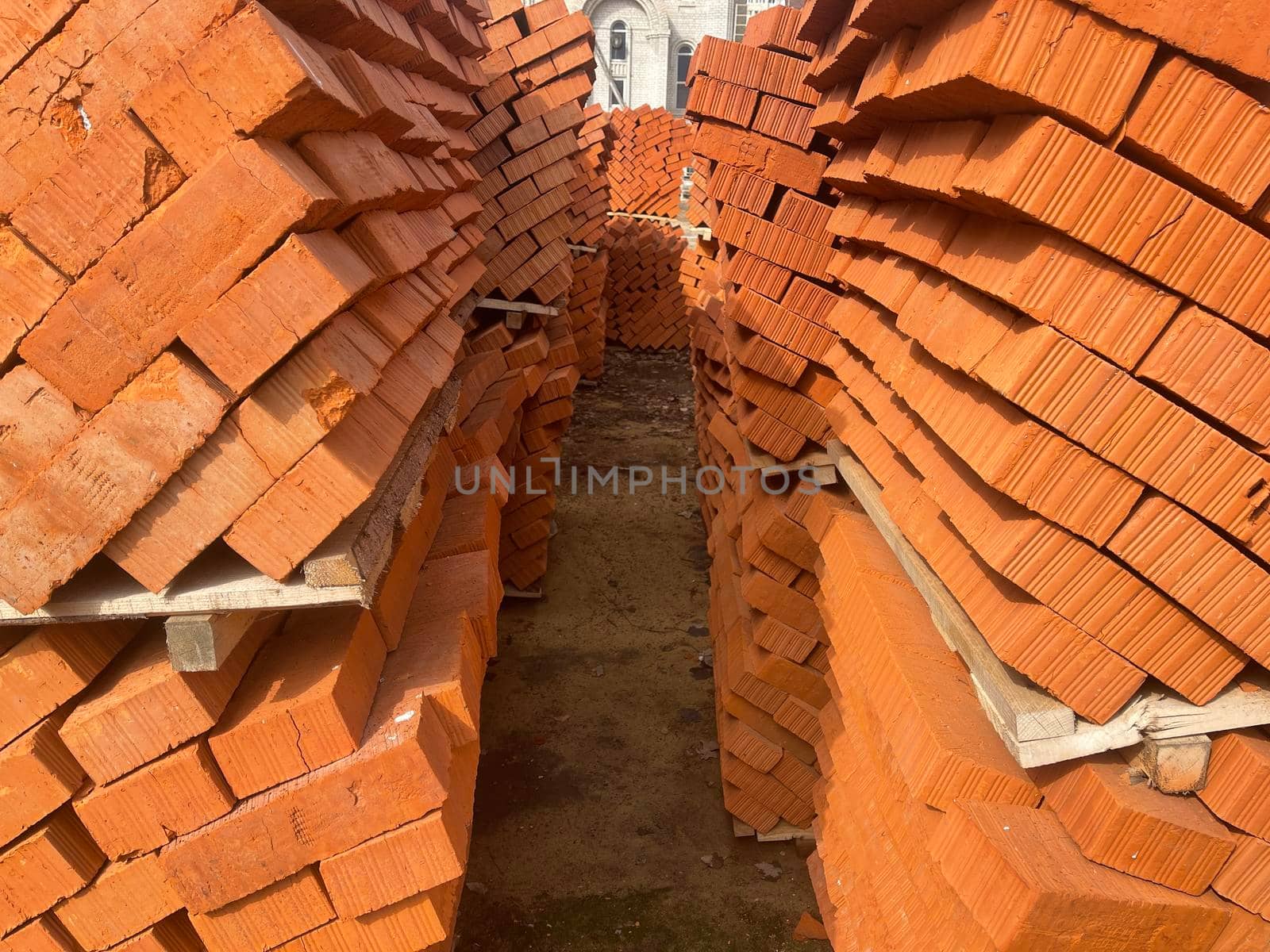 Pile of pallets with red bricks on city street. Building materials on construction site outdoor. Concept of constructing buildings. by epidemiks