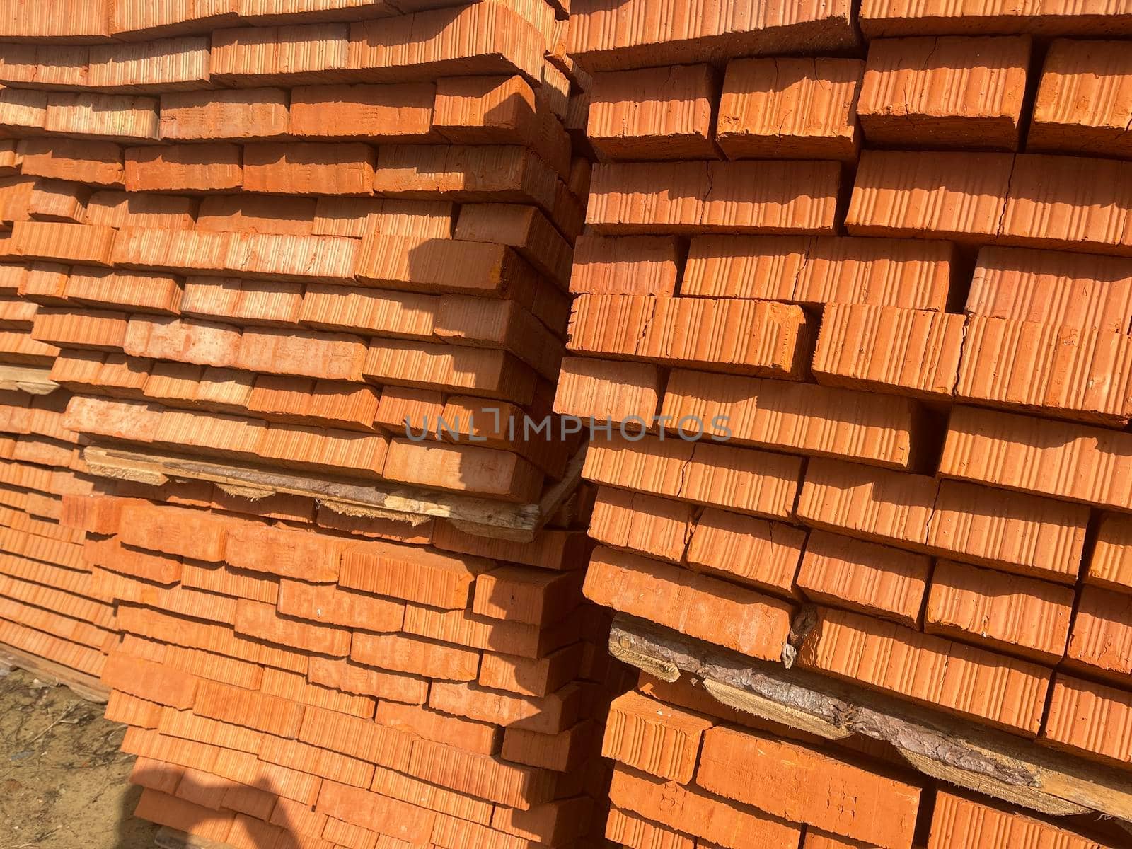 Pile of pallets with red bricks on city street. Building materials on construction site outdoor. Concept of constructing buildings