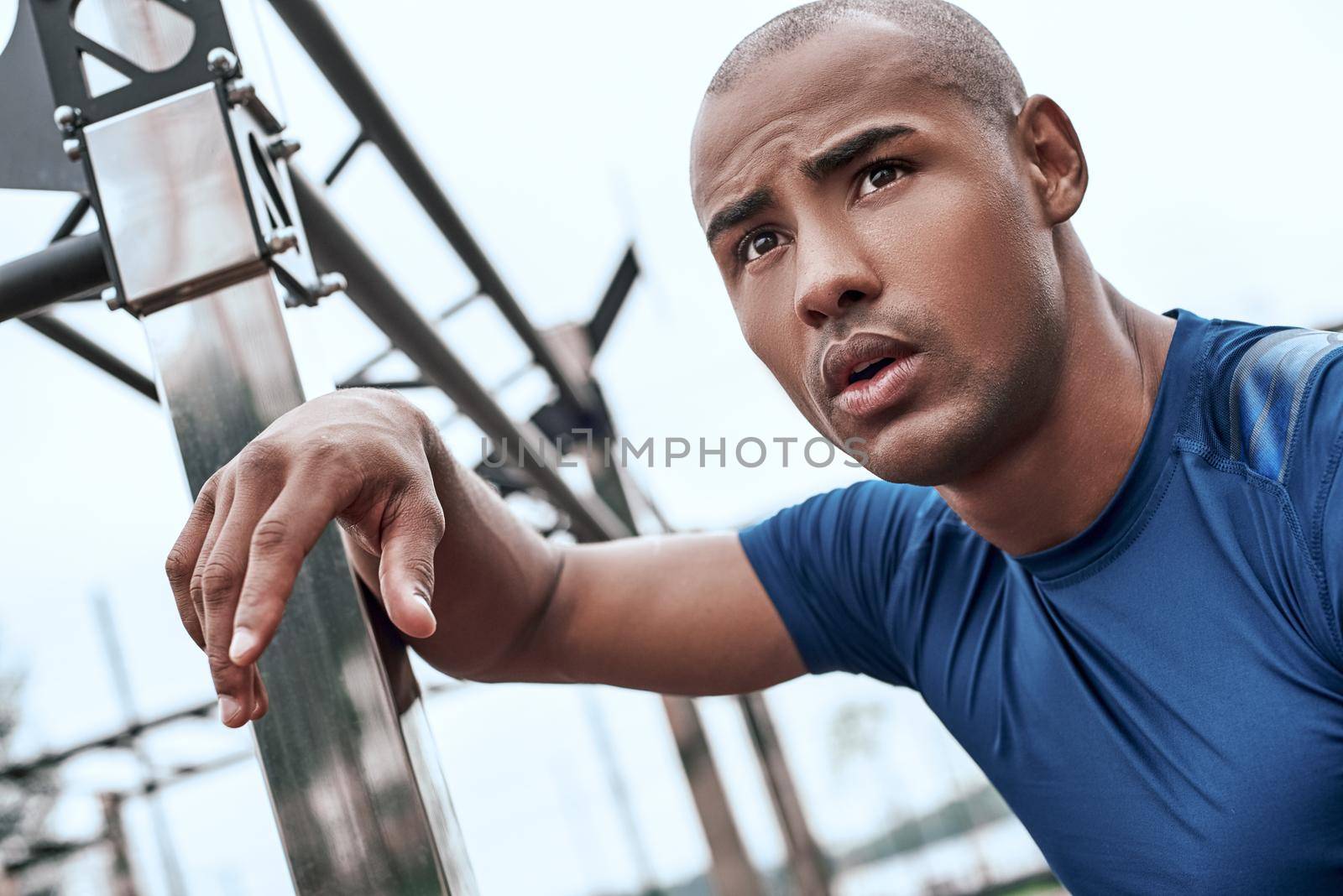 Young african man at the open air gym is resting after doing exercises by friendsstock
