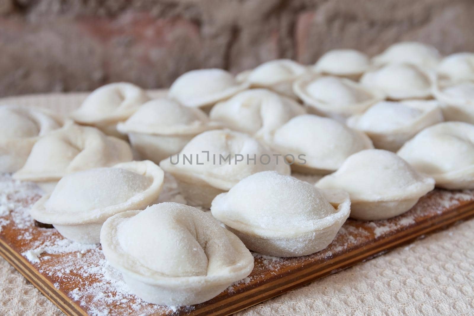 Process of making homemade pelmeni on wooden board. Traditional dish of Russian cuisine. Selective focus