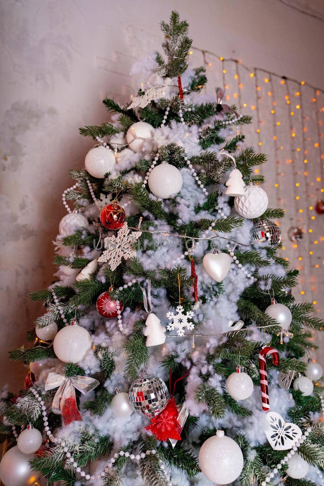 Decorated Christmas tree in the room. Coniferous tree with white and red baubles located near the white wall during the celebration of the holiday by epidemiks
