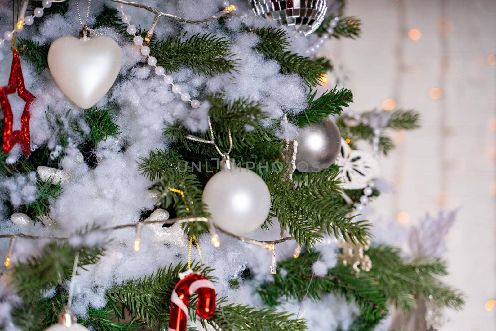 Decorated Christmas tree in the room. Coniferous tree with white and red baubles located near the white wall during the celebration of the holiday by epidemiks