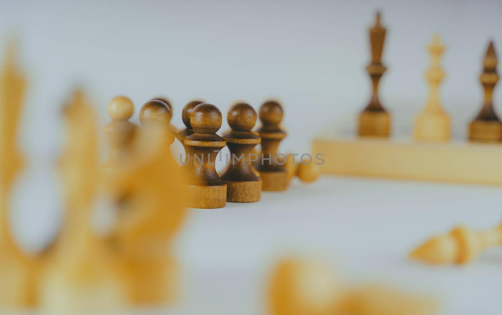 Close up of rows of black and white wooden chess pieces on white background. Selective focus on black pawns. by epidemiks