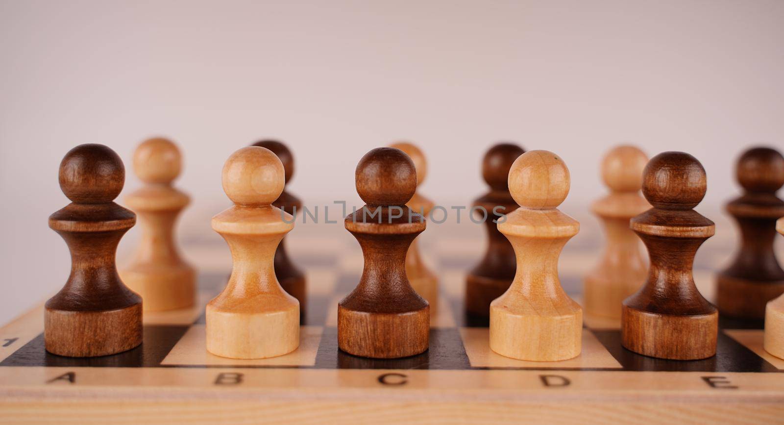Close up of black and white wooden chess pieces on white background. Selective focus on black pawn. by epidemiks