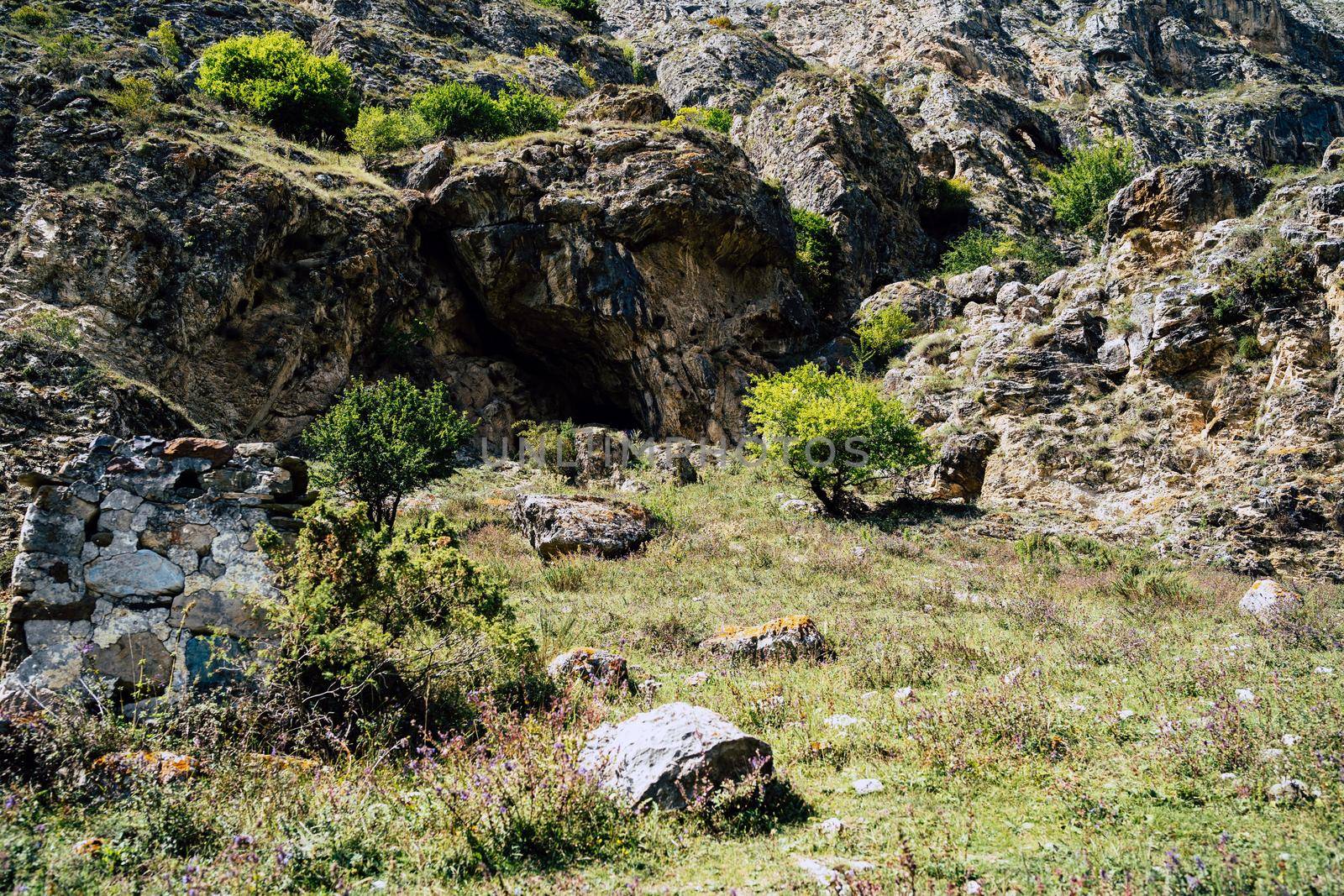 Small cave in rock on sunny day. Uneven mountain with cave and green vegetation in summertime. by epidemiks