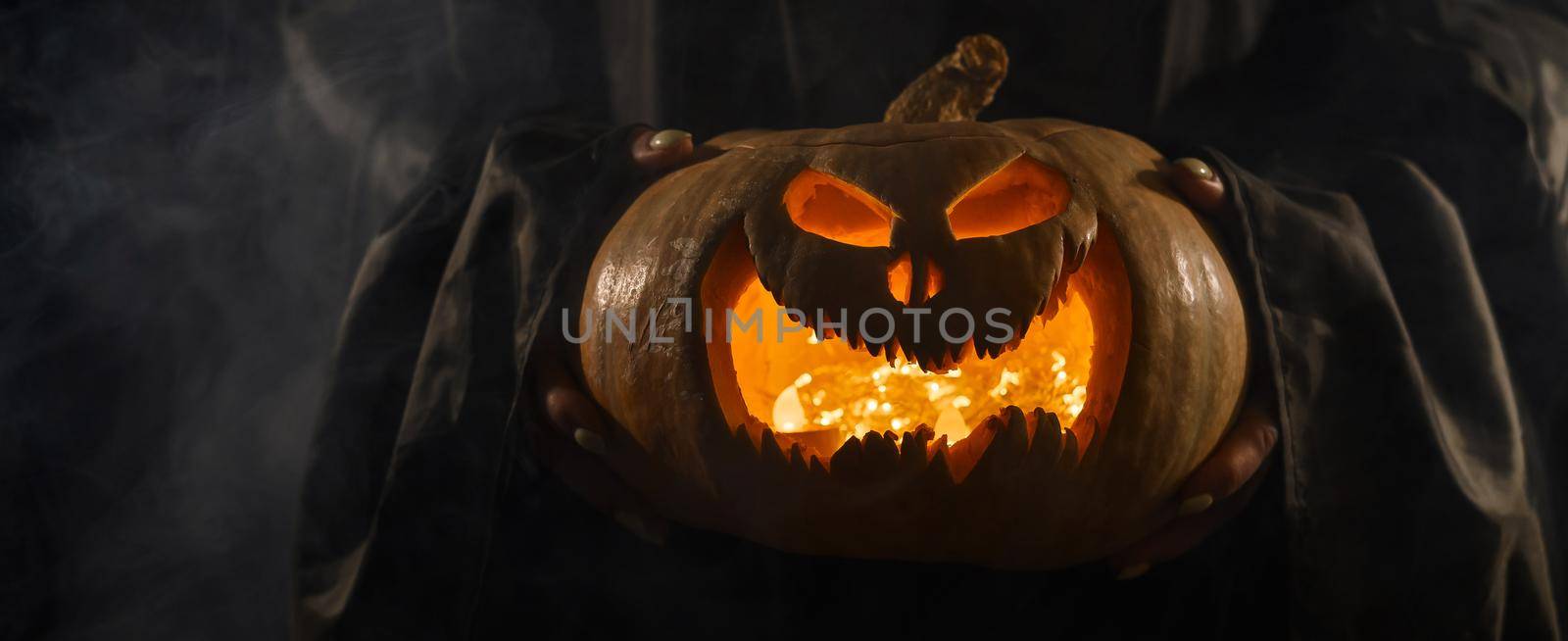 The witch is holding a pumpkin jack o lantern glowing in the dark. Halloween. by mrwed54