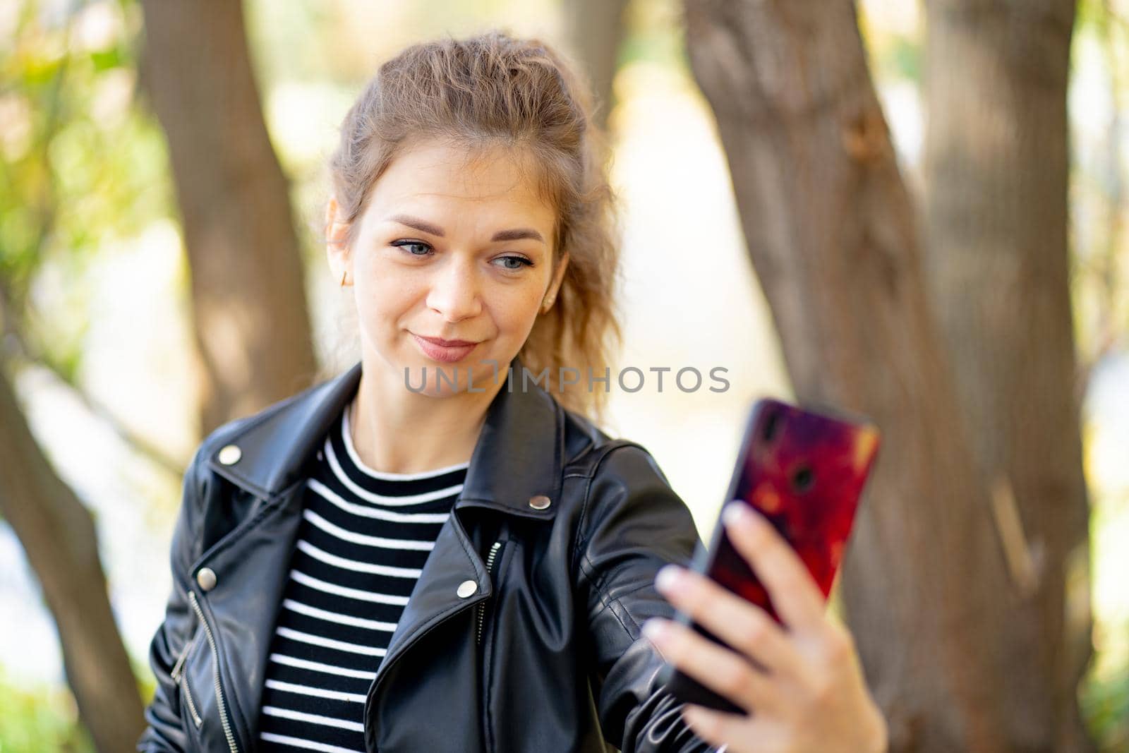 Young woman using smartphone in park. Smiling young female with long hair waving in wind browsing mobile phone while spending autumn day in park by epidemiks
