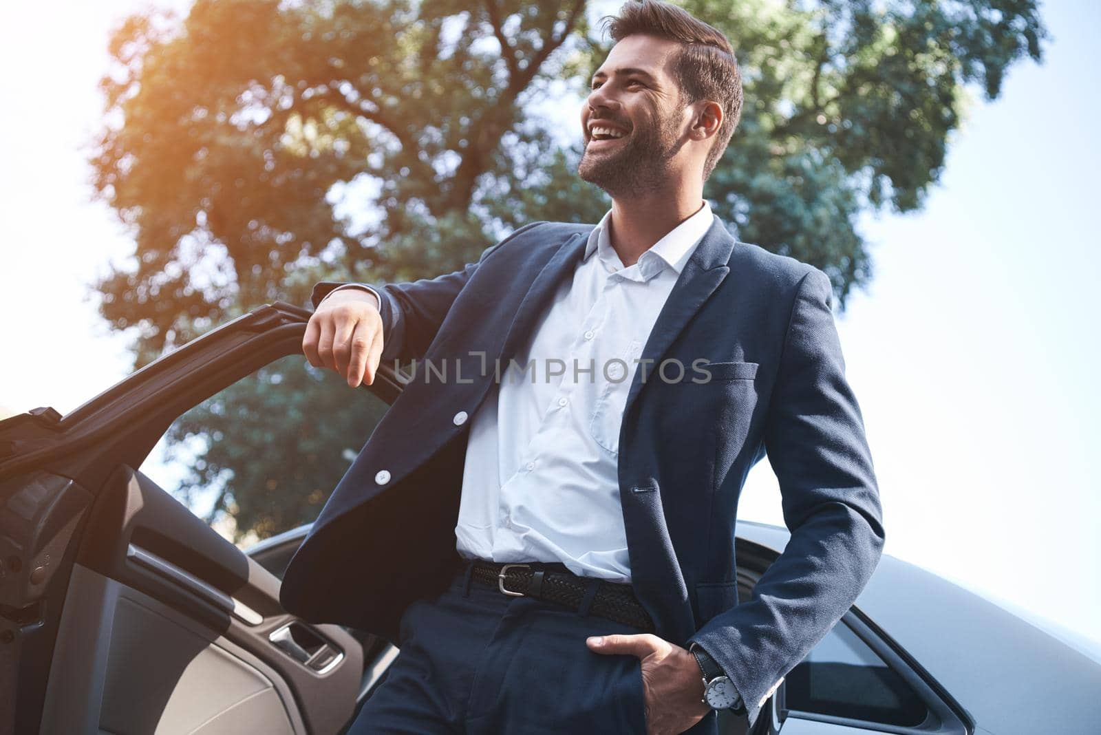 A young handsome man in a suit comes out of the car and laughs by friendsstock