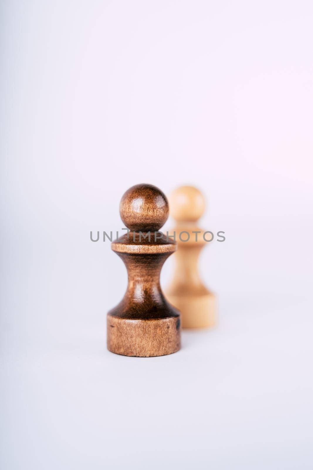 Close up of rows of black and white wooden chess pieces on white background. Selective focus on black pawns. by epidemiks