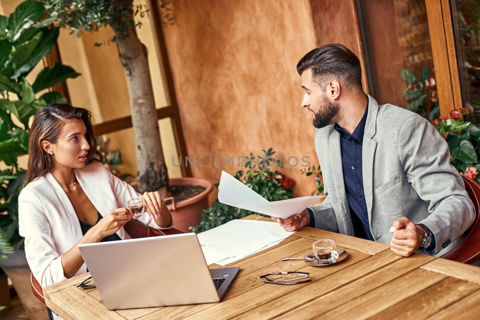 Business lunch. Man and woman sitting at table at restaurant discussing project lively by friendsstock