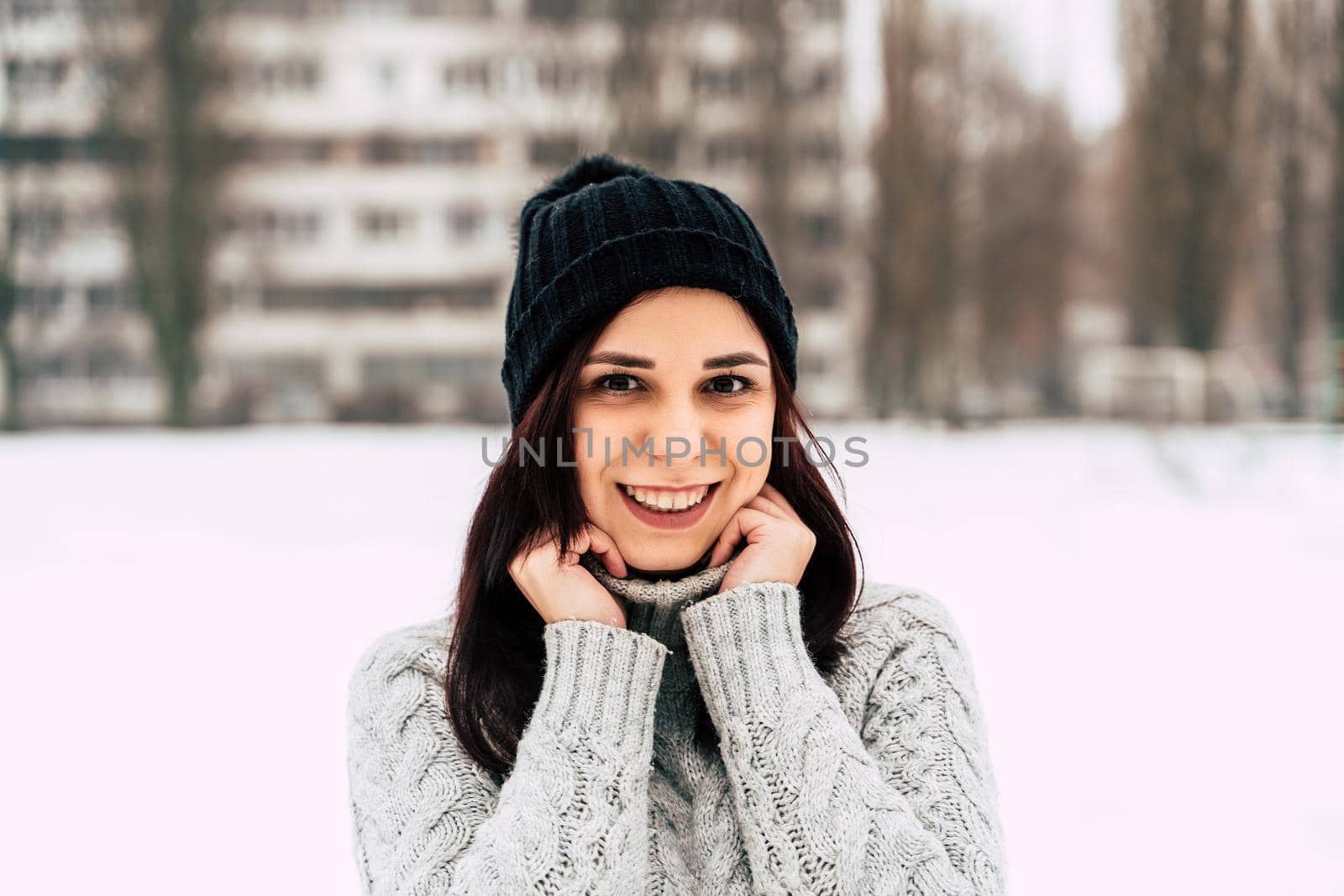Young, beautiful woman with winter cap and gray sweater smiling and laughing while standing outside in winter by epidemiks