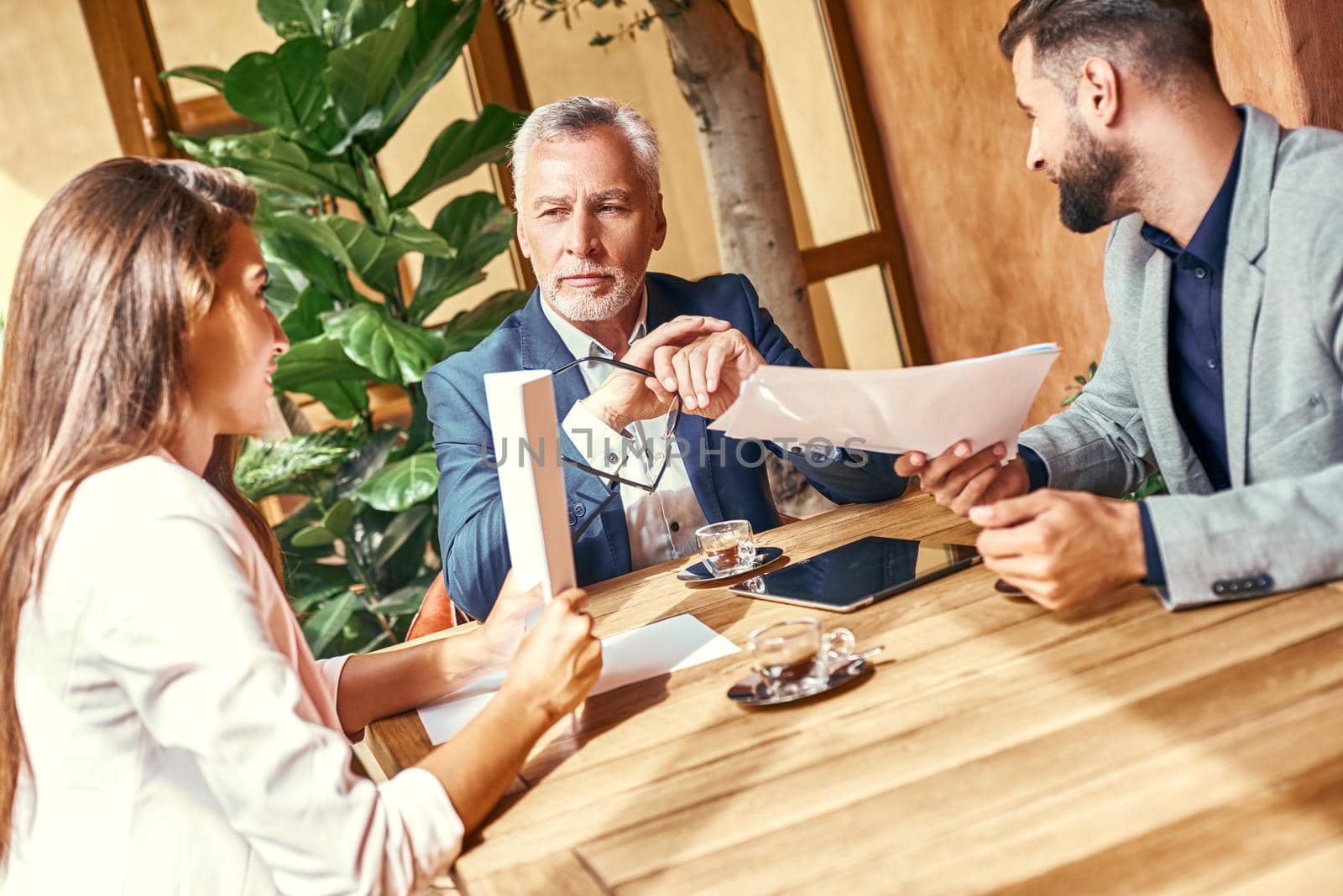 Business lunch. Three people in the restaurant sitting at table discussing project concentrated. Team work concept by friendsstock