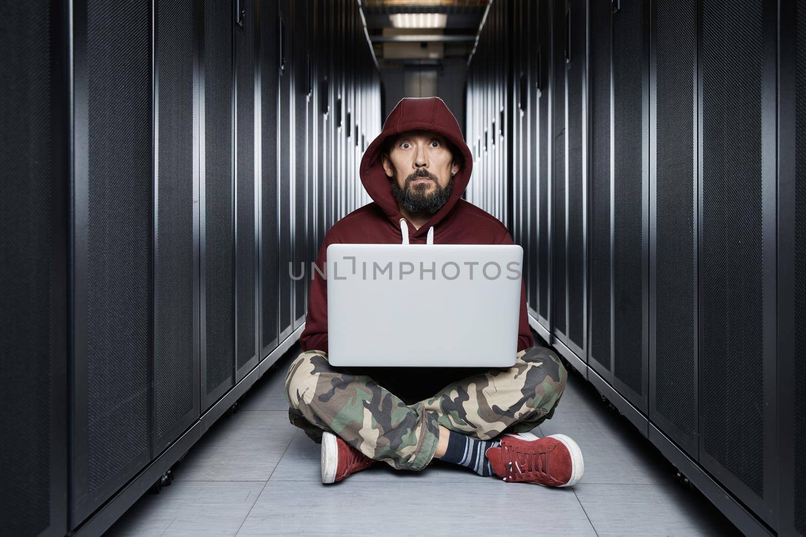 The hacker in a hood sits with the computer among servers, the burglar. Storage of data, cloudy services, system breaking, attack of hackers. High quality photo