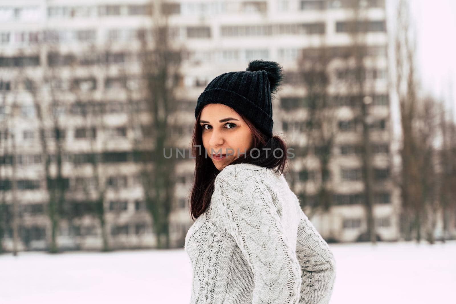 Young, beautiful woman with winter cap and gray sweater standing outside in winter