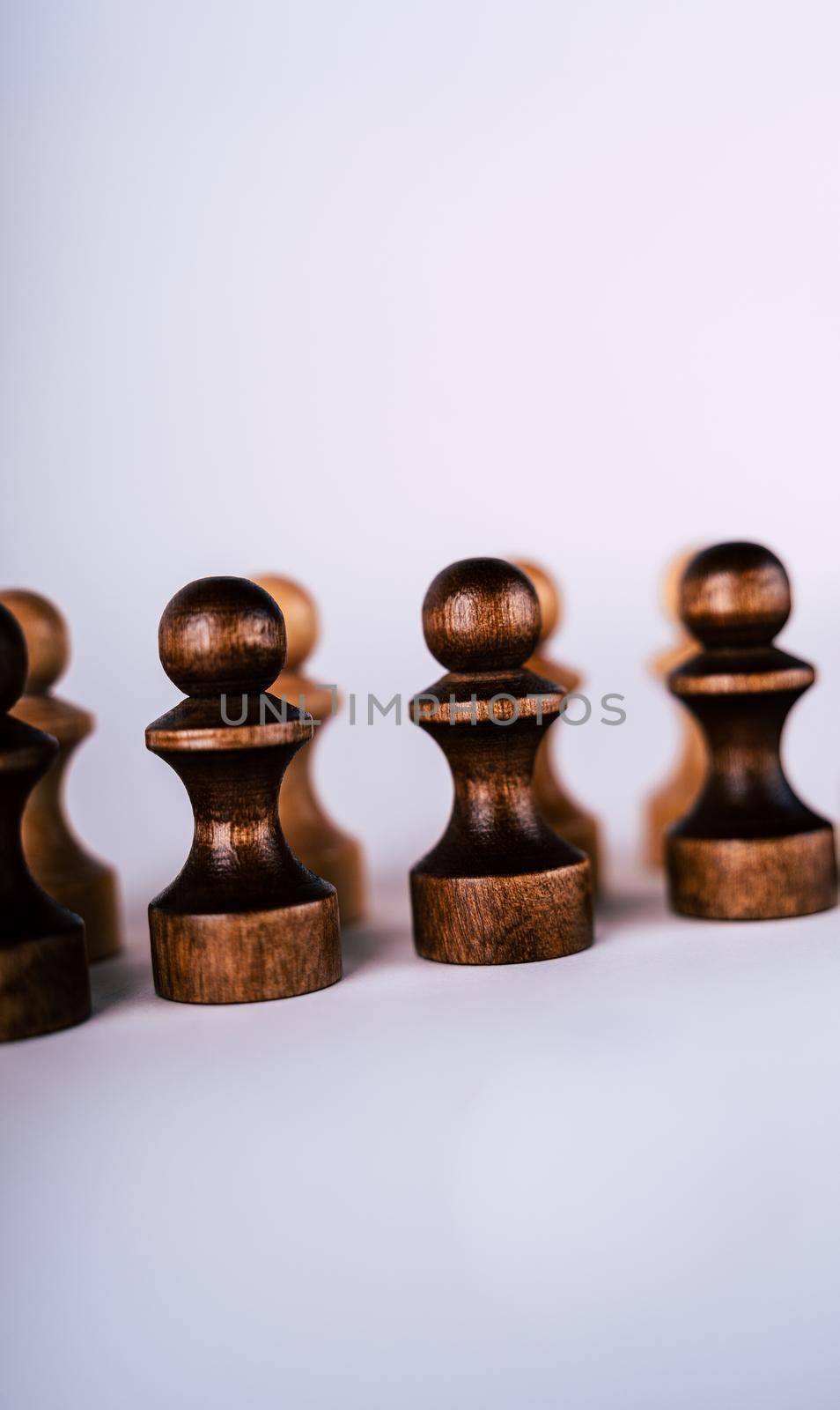 Close up of rows of black and white wooden chess pieces on white background. Selective focus on black pawns