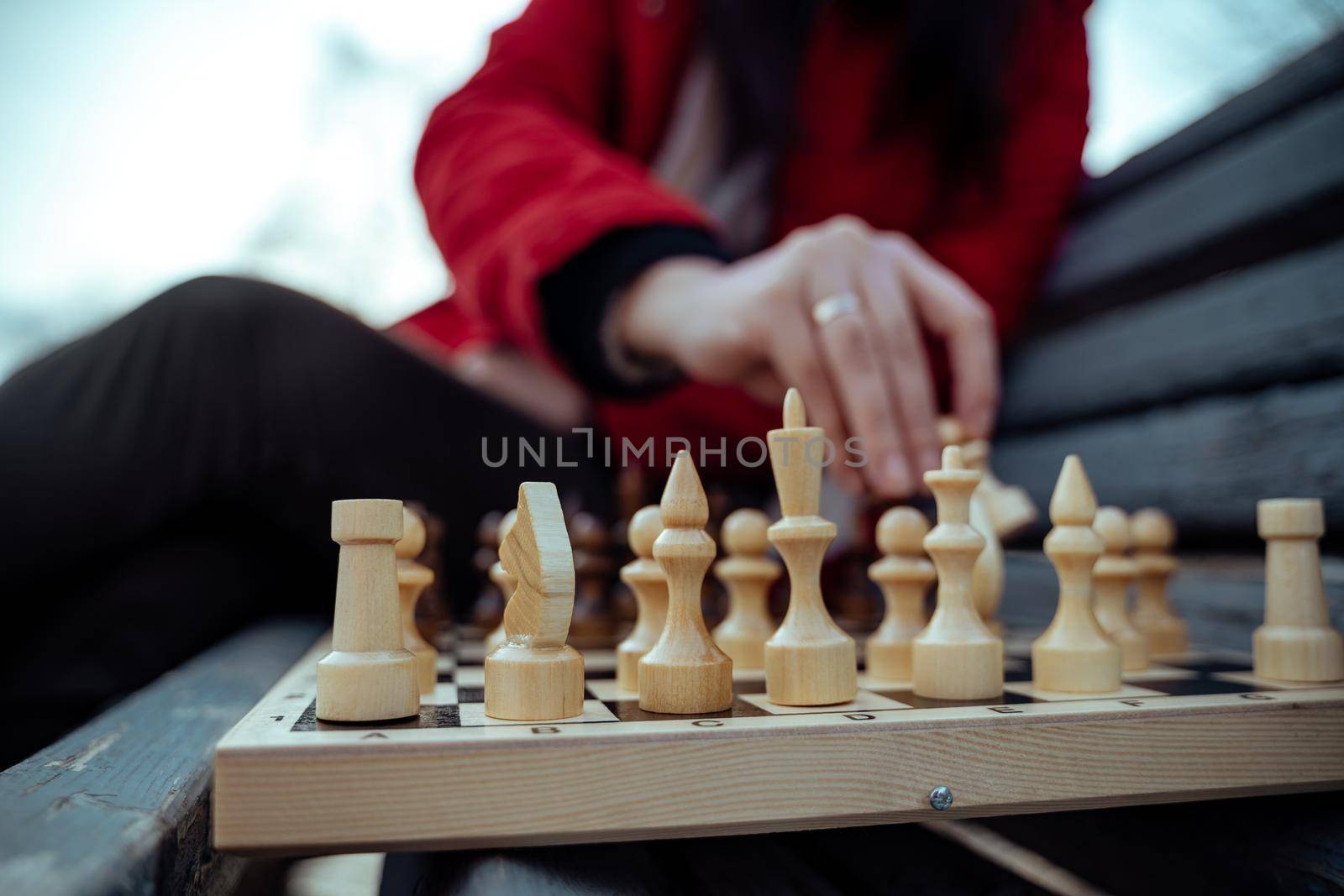 Close up of chess on wooden bench. Body part of unrecognizable woman playing in board game in city park. by epidemiks