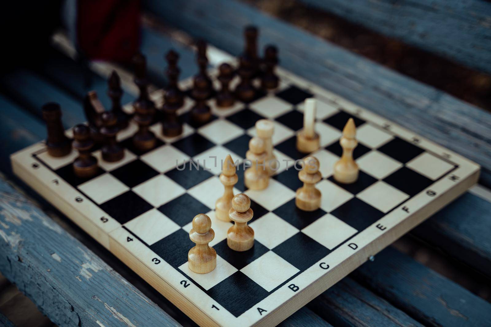 Close up of chess on wooden bench. Body part of unrecognizable woman playing in board game in city park. by epidemiks