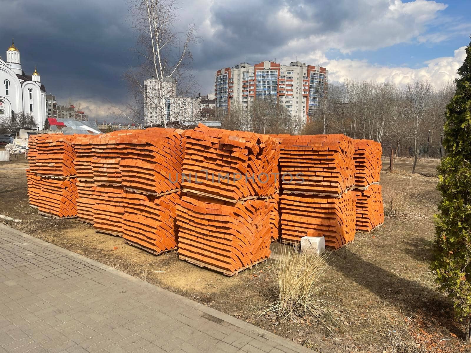 Pile of pallets with red bricks on city street. Building materials on construction site outdoor. Concept of constructing buildings