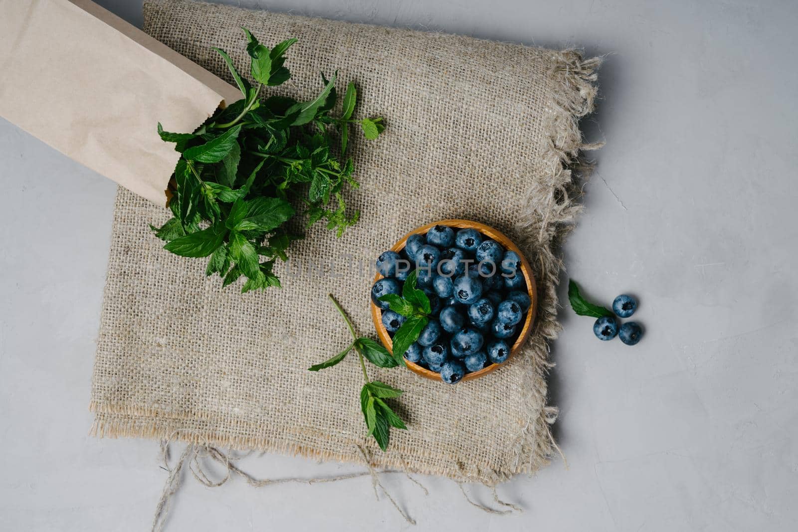 A small wooden bowl with berries. Juicy and ripe blueberries in an eco-friendly dish. Sprigs of fresh mint in a kraft bag. The concept of healthy eating and nutrition