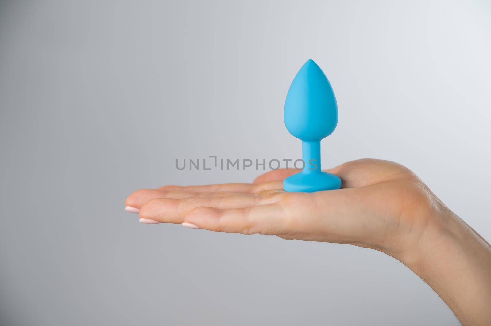 Woman holding a blue anal plug on a white background. Adult toy for alternative sex.