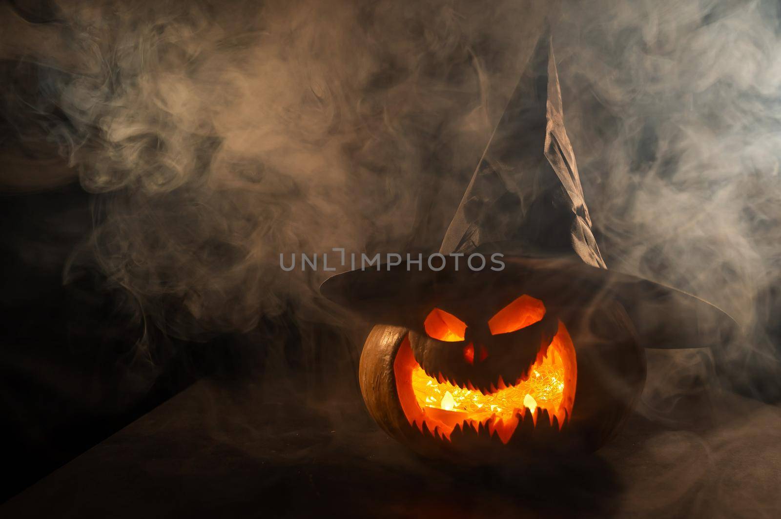 A creepy pumpkin with a carved grimace in the smoke. Jack o lantern in the dark